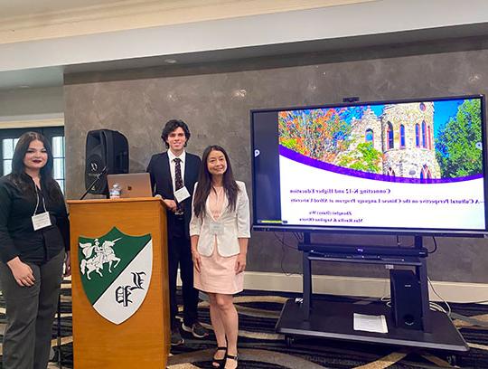 two women and a man standing by a lectern and projector screen